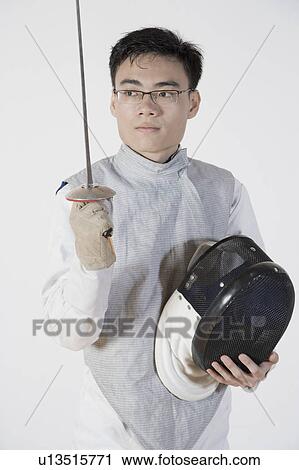 Stock Image - Close-up of a male fencer holding a fencing mask and a fencing foil. Fotosearch