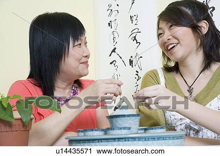 Stock Image - Close-up of a mature woman sitting with her daughter at a table and holding tea cups. Fotosearch