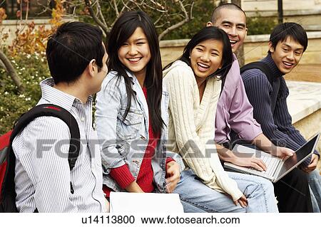 Stock Image - Five young college students sitting together in a college campus and smiling. Fotosearch