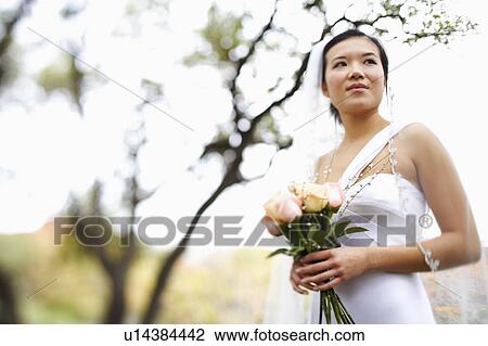 Stock Image - Low angle view of a bride holding a bouquet of flowers. Fotosearch