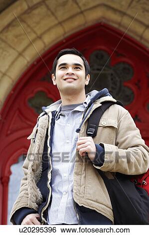 Low angle view of a young man carrying a backpack and smiling View Large Photo Image Stock Photograph - Low angle view of a young man carrying a backpack and smiling. Fotosearch