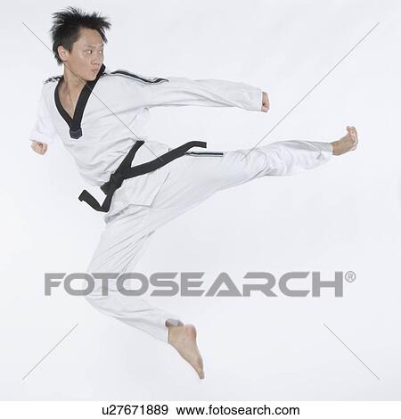 Stock Photo - Mid adult man performing flying kick. Fotosearch