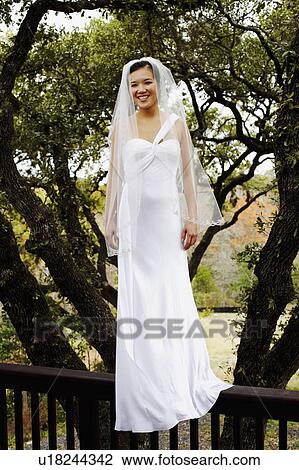 Stock Image - Portrait of a bride standing on a railing and smiling. Fotosearch