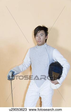 Stock Image - Portrait of a male fencer holding a sword and a fencing mask. Fotosearch