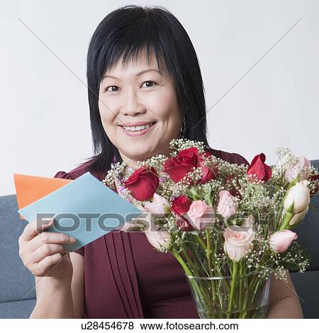 Stock Photo - Portrait of a mature woman holding a greeting card and a flower vase. Fotosearch