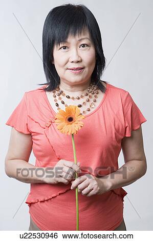 Portrait of a mature woman holding a daisy flower View Large Photo Image Stock Photograph - Portrait of a mature woman holding a daisy flower. Fotosearch