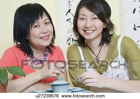 Portrait of a mature woman sitting with her daughter at a table and holding tea cups View Large Photo Image Stock Photograph - Portrait of a mature woman sitting with her daughter at a table and holding tea cups. Fotosearch