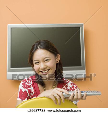 Portrait of a young woman holding a remote control and smiling View Large Photo Image Stock Photo - Portrait of a young woman holding a remote control and smiling. Fotosearch