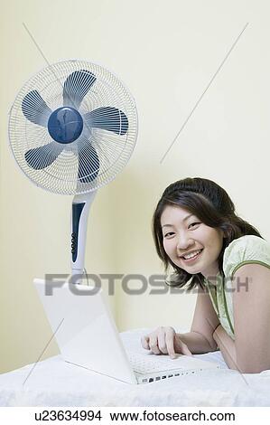 Picture - Portrait of a young woman lying on the bed and using a laptop. Fotosearch