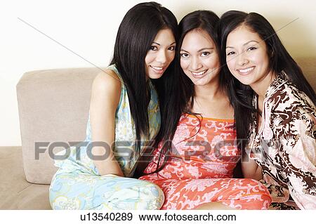 Stock Photo - Portrait of three young women sitting on a couch and smiling. Fotosearch