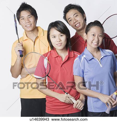 Stock Image - Portrait of two young couples holding badminton rackets and smiling. Fotosearch