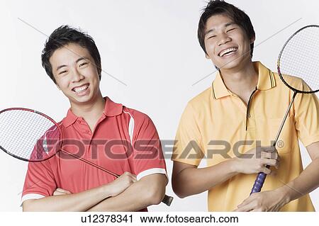 Stock Image - Portrait of two young men holding badminton rackets and smiling. Fotosearch
