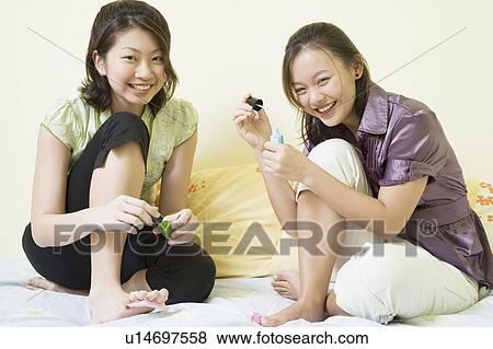 Portrait of two young women applying nail polish on their toenails View Large Photo Image Stock Photo - Portrait of two young women applying nail polish on their toenails. Fotosearch