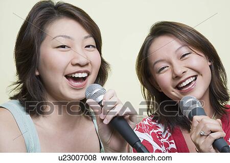Stock Photo - Portrait of two young women singing together into microphones. Fotosearch
