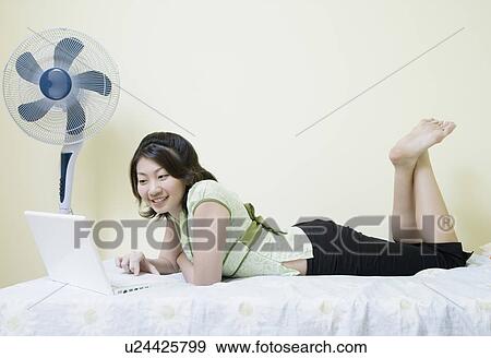 Stock Photo - Side profile of a young woman lying on the bed and using a laptop. Fotosearch