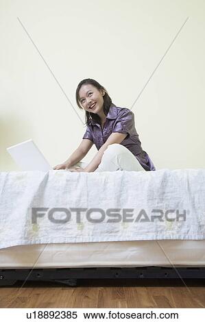 Side profile of a young woman sitting cross-legged on the bed and using a laptop View Large Photo Image Stock Photography - Side profile of a young woman sitting cross-legged on the bed and using a laptop. Fotosearch