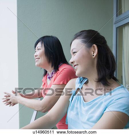 Side profile of a young woman standing in a balcony with her mother and smiling View Large Photo Image Stock Image - Side profile of a young woman standing in a balcony with her mother and smiling. Fotosearch