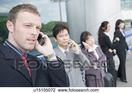 Stock Image - Three businesswomen with two businessmen waiting at an airport lounge. Fotosearch