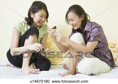 Stock Image - Two young women applying nail polish on their toenails. Fotosearch
