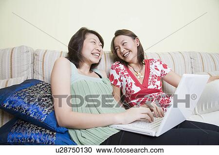 Two young women laughing and using a laptop View Large Photo Image Stock Image - Two young women laughing and using a laptop. Fotosearch