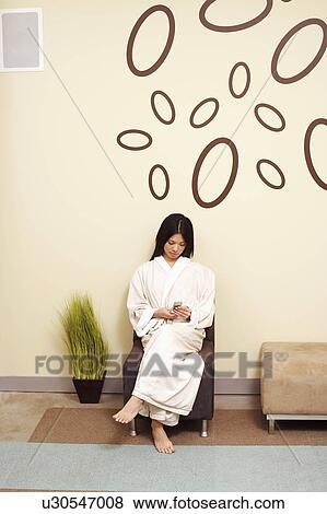 Young woman sitting on a chair and using a mobile phone View Large Photo Image Stock Photo - Young woman sitting on a chair and using a mobile phone. Fotosearch