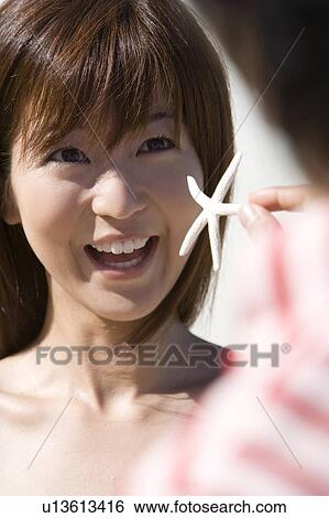 Stock Photograph - Man showing woman dead starfish, woman smiling, differential focus, Saipan, USA . Fotosearch