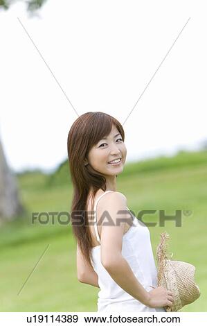 Stock Photo - Portrait of a young woman standing on lawn, holding a straw hat, differential focus, Saipan, USA . Fotosearch