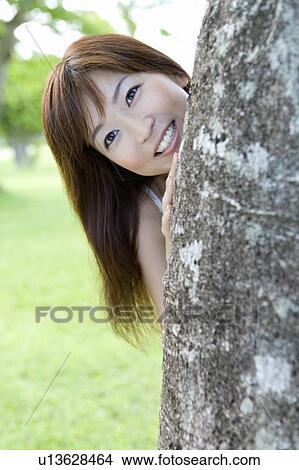 Picture - Portrait of a young woman standing behind a tree, smiling, Saipan, USA . Fotosearch