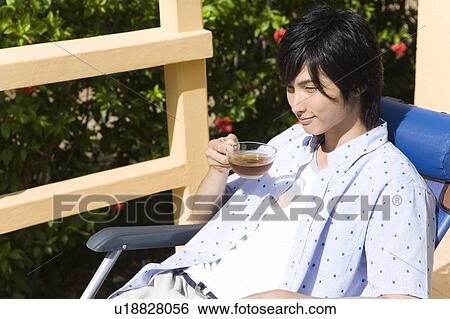 Stock Photograph - Young man sipping tea at balcony, Saipan. Fotosearch