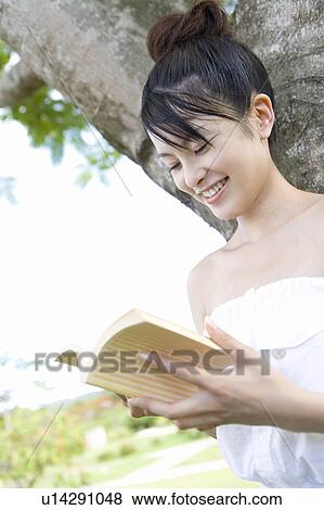 Young woman leaning on tree trunk and reading a book, smiling, Saipan, USA View Large Photo Image Stock Photo - Young woman leaning on tree trunk and reading a book, smiling, Saipan, USA . Fotosearch