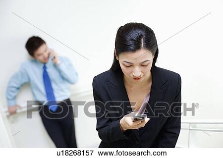 Stock Photo - Businesswoman operating a mobile phone with a businessman standing behind her. Fotosearch
