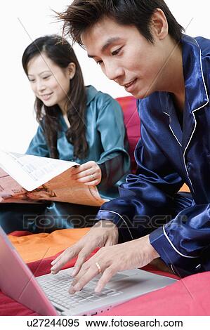Stock Photography - Close-up of a mid adult man using a laptop and young woman reading a newspaper. Fotosearch