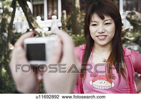 Stock Image - Close-up of a person's hand taking a photograph of a young woman smiling. Fotosearch