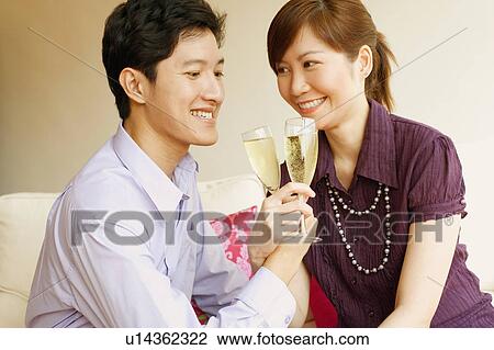 Stock Image - Close-up of a young couple smiling and toasting champagne flutes. Fotosearch