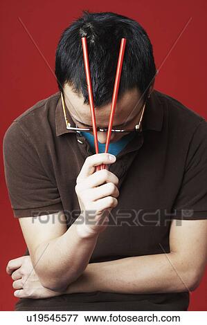 Stock Photo - Close-up of a young man holding chopsticks on his head. Fotosearch