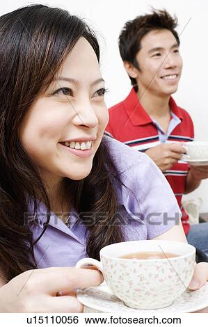 Stock Photograph - Close-up of a young woman and a mid adult man drinking tea. Fotosearch