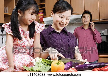 Close-up of a young woman cutting vegetables with her daughter sitting beside her View Large Photo Image Stock Image - Close-up of a young woman cutting vegetables with her daughter sitting beside her. Fotosearch