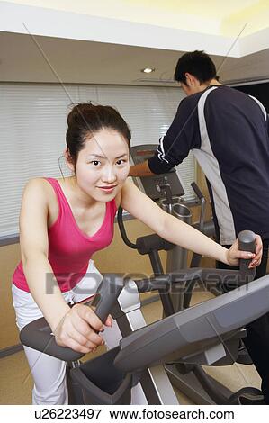 Stock Photo - Close-up of a young woman exercising in a gym with a young man. Fotosearch