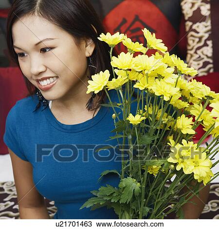 Stock Image - Close-up of a young woman holding a flower vase and smiling. Fotosearch