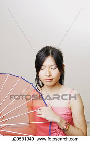 Stock Photo - Close-up of a young woman holding a parasol with her eyes closed. Fotosearch