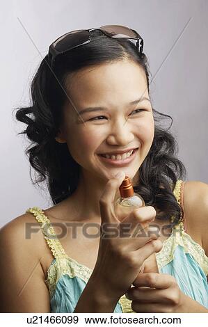 Close-up of a young woman holding a bottle of perfume and smiling View Large Photo Image Stock Photo - Close-up of a young woman holding a bottle of perfume and smiling. Fotosearch