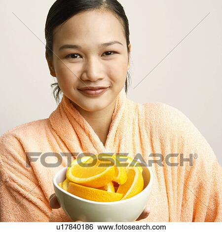 Stock Photograph - Close-up of a young woman holding a bowl of orange slices. Fotosearch