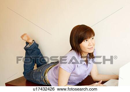 Close-up of a young woman lying on a table and using a laptop View Large Photo Image Stock Photograph - Close-up of a young woman lying on a table and using a laptop. Fotosearch