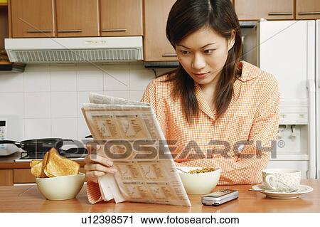Close-up of a young woman reading a newspaper at a kitchen counter View Large Photo Image Stock Image - Close-up of a young woman reading a newspaper at a kitchen counter. Fotosearch