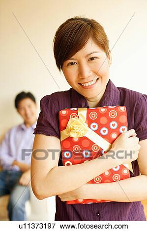 Stock Photo - Close-up of a young woman smiling and holding a gift. Fotosearch