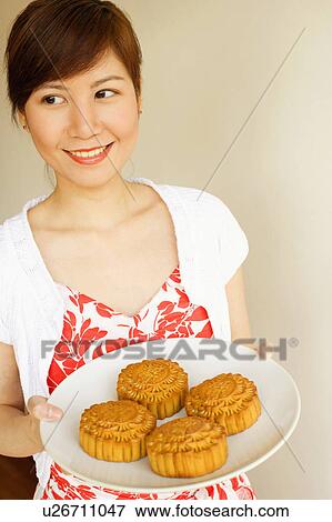 Stock Photo - Close-up of a young woman standing and holding a plate of cake. Fotosearch