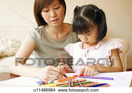 Picture - Close-up of a young woman teaching her daughter to color. Fotosearch