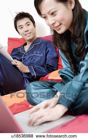 Stock Photo - Close-up of a young woman using a laptop and mid adult man holding a newspaper. Fotosearch
