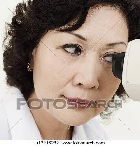 Stock Image - Close-up of an optometrist looking into an ophthalmoscope. Fotosearch
