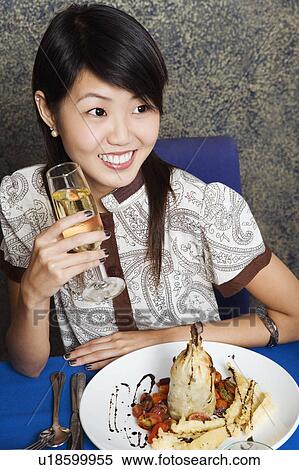Stock Photography - High angle view of a young woman holding a glass of champagne in a restaurant. Fotosearch